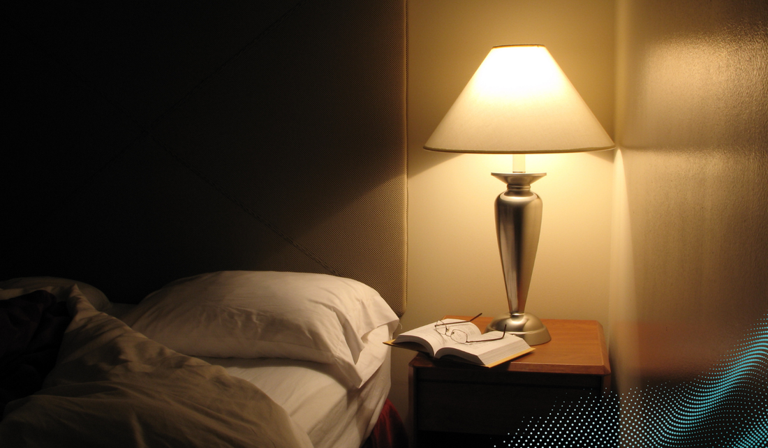 A lamp is dimly lit sat on a bedside cabinet 