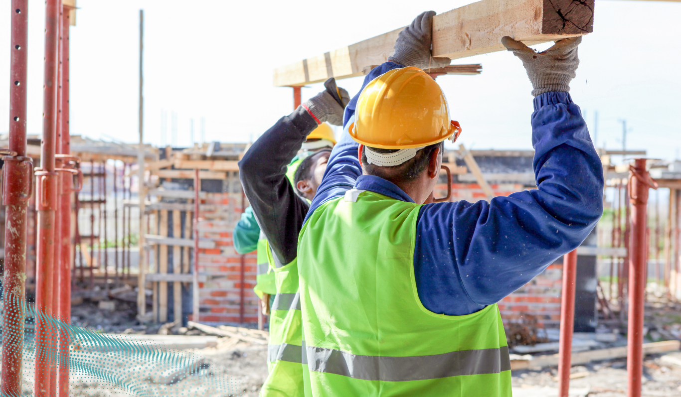 two site workers carrying a long wooden beam overhead