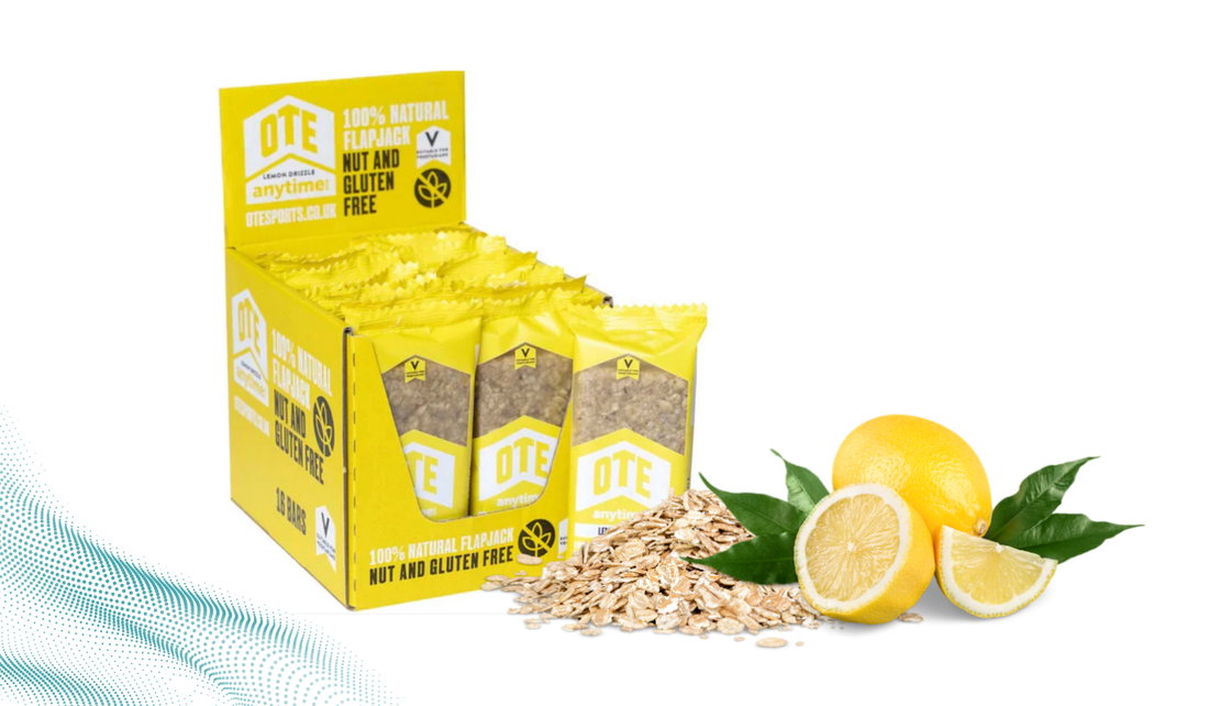 Bright yellow display box of OTE Anytime lemon drizzle flapjack bars, showing individually wrapped bars labeled “100% natural, nut and gluten free,” alongside oats and whole and sliced lemons on a white background